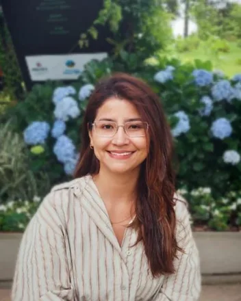 Foto de Indaia Lima, sorrindo, de óculos, com hortênsias ao fundo